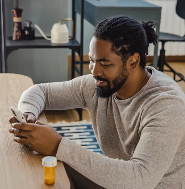 Man sitting at a table using his smartphone with a prescription pill bottle beside him.